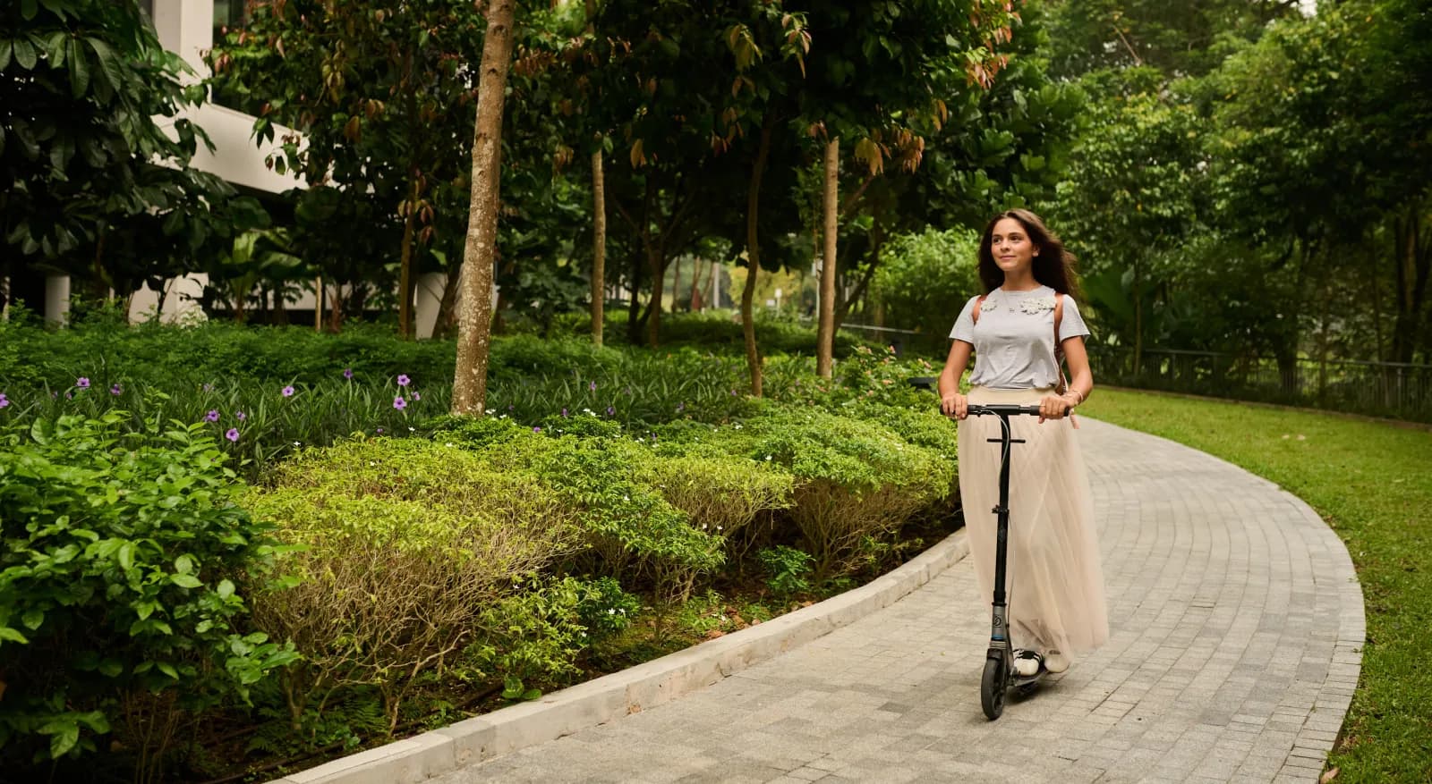 A girl riding a scooter along a curving garden path